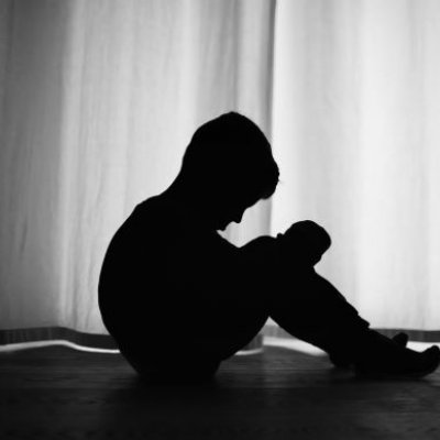 A profile photo in shadow of a young boy seated and looking down dejectedly.